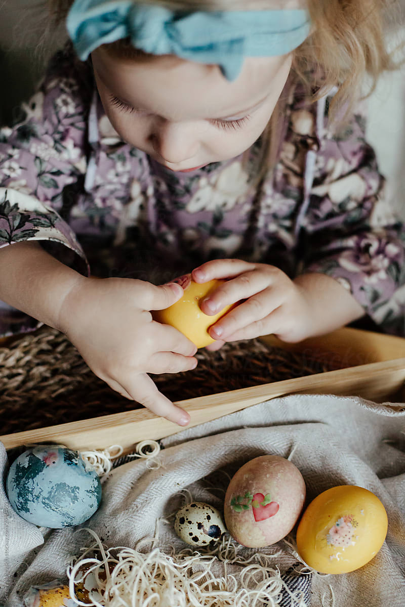 Little girl decorating egg with sticker on Easter