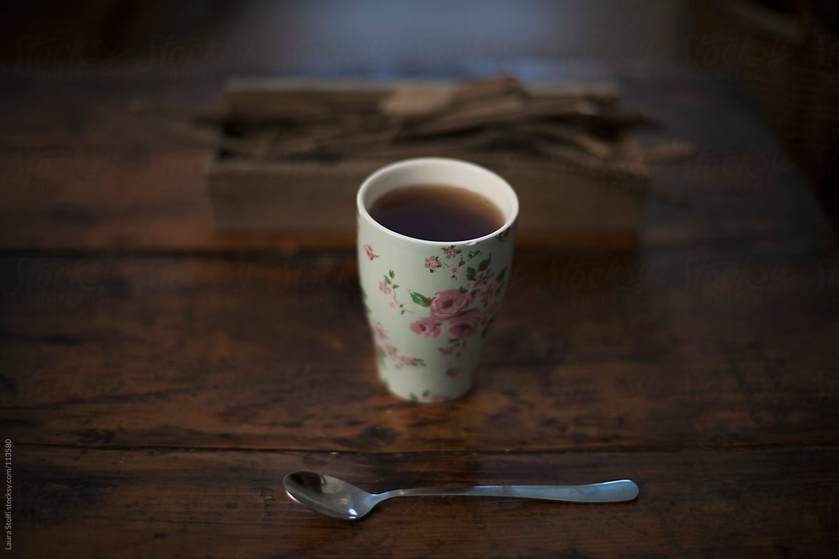 A flowered tea mug close to spoon and wooden sticks on table