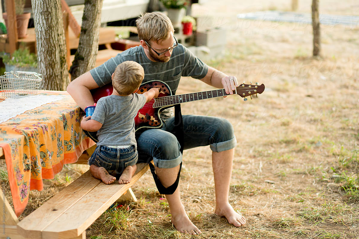 Father and son play guitar on picnic bench