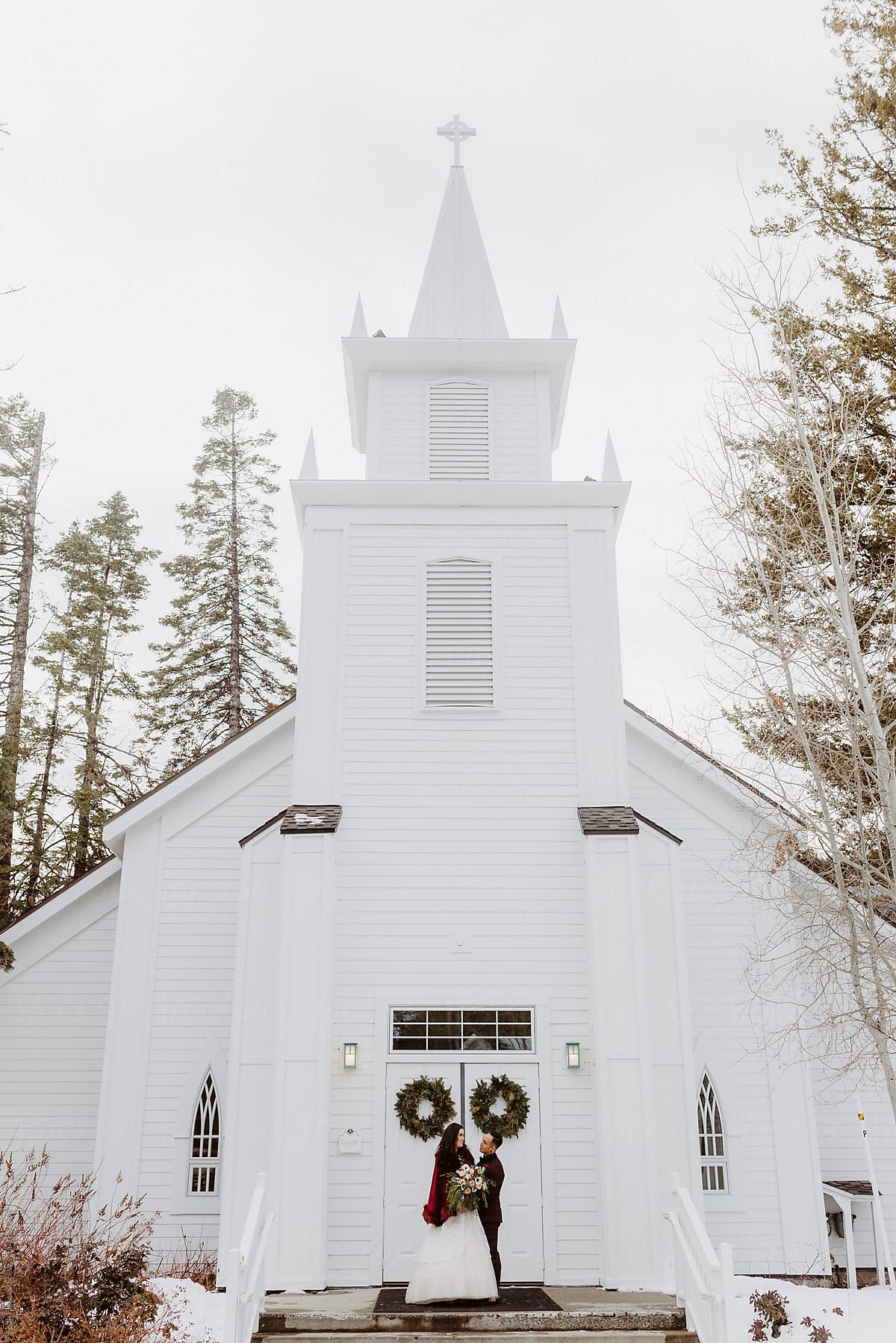 Bride and Groom Standing in front of White Chapel in Winter Landscape after Wedding Ceremony