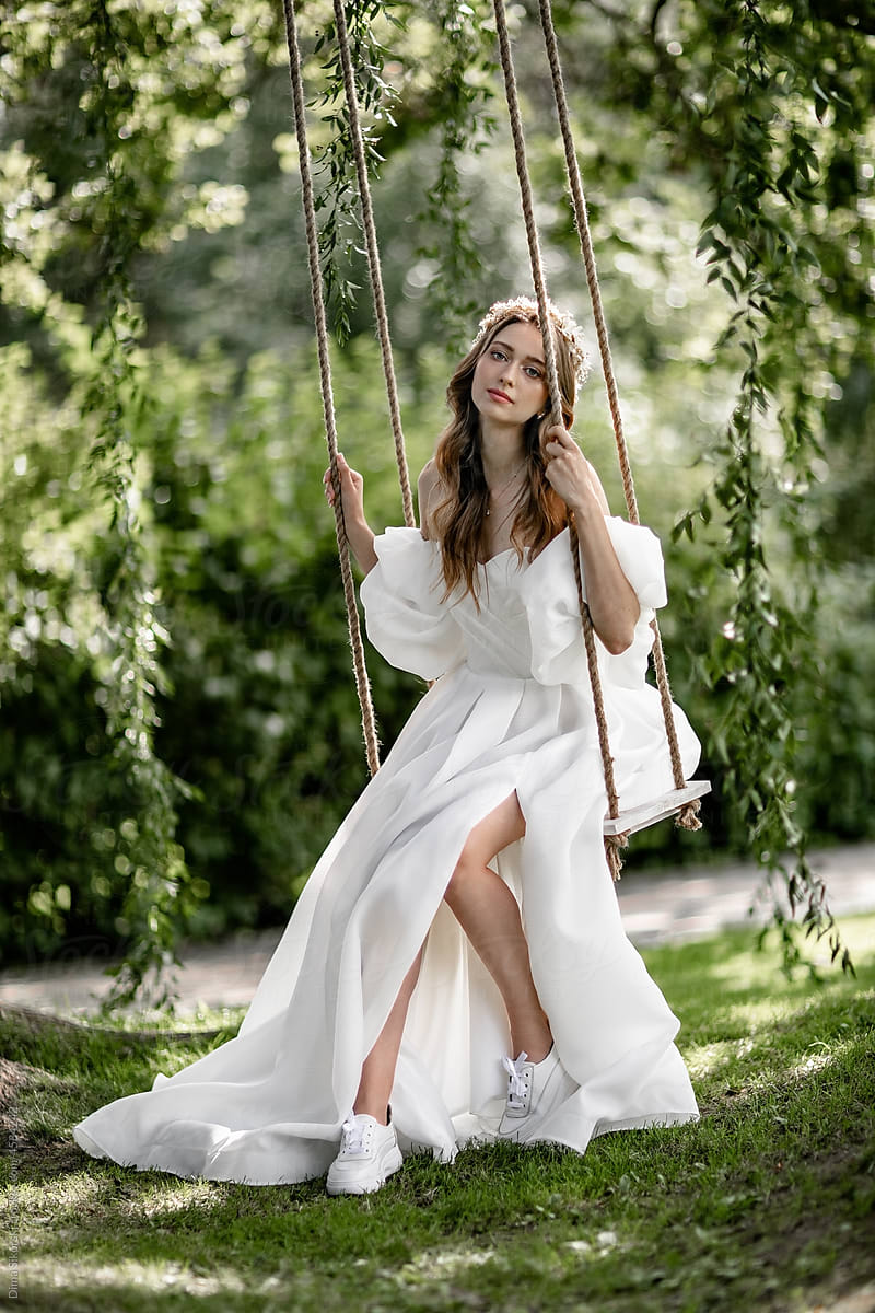 The bride in an elegant light dress is sitting on a rope swing