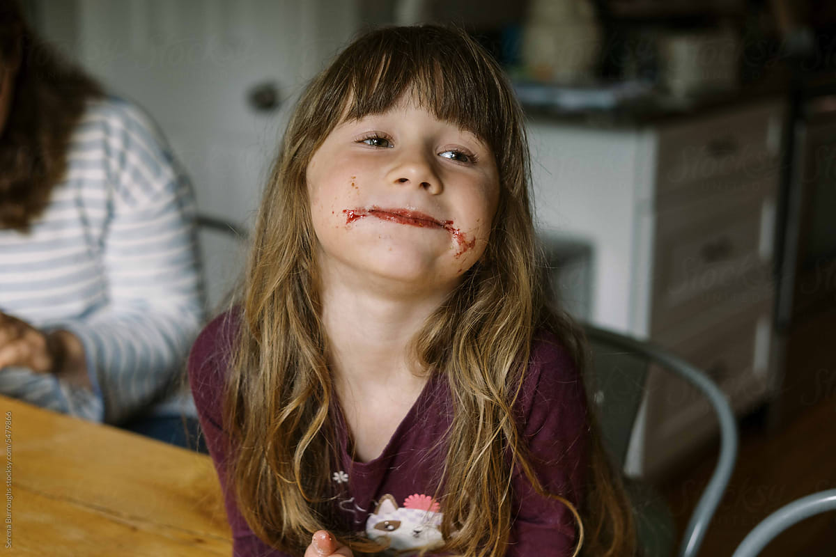 little girl with jam on her cheeks smiling at the table