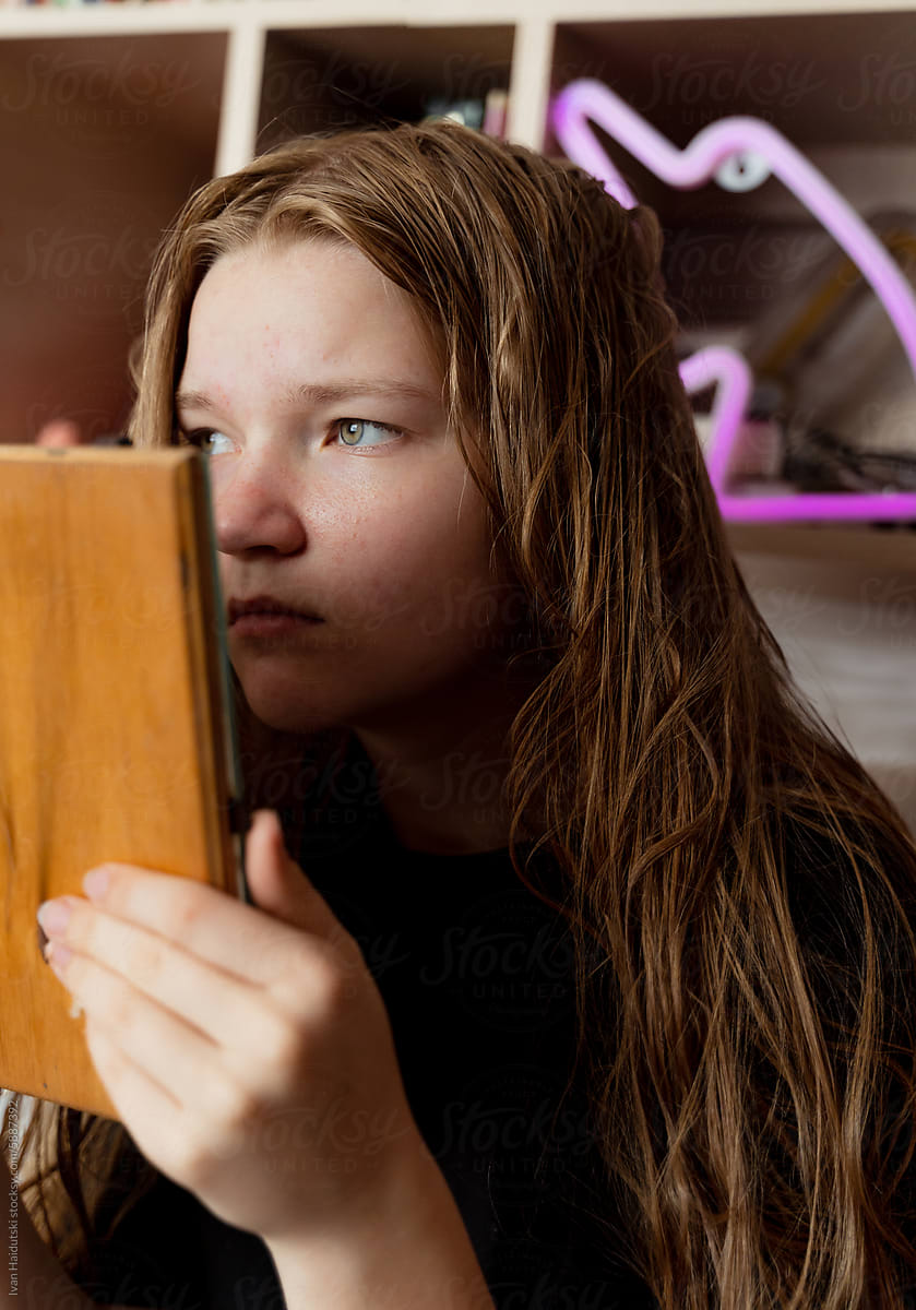 Teen girl sadly examines acne in mirror, facial concerns