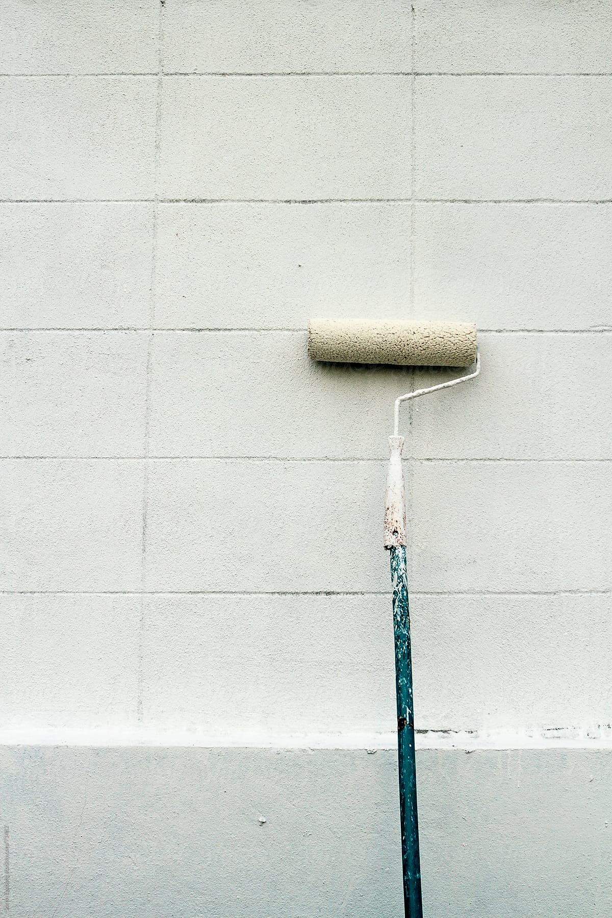 White paint roller with bue shaft leaning against white wall