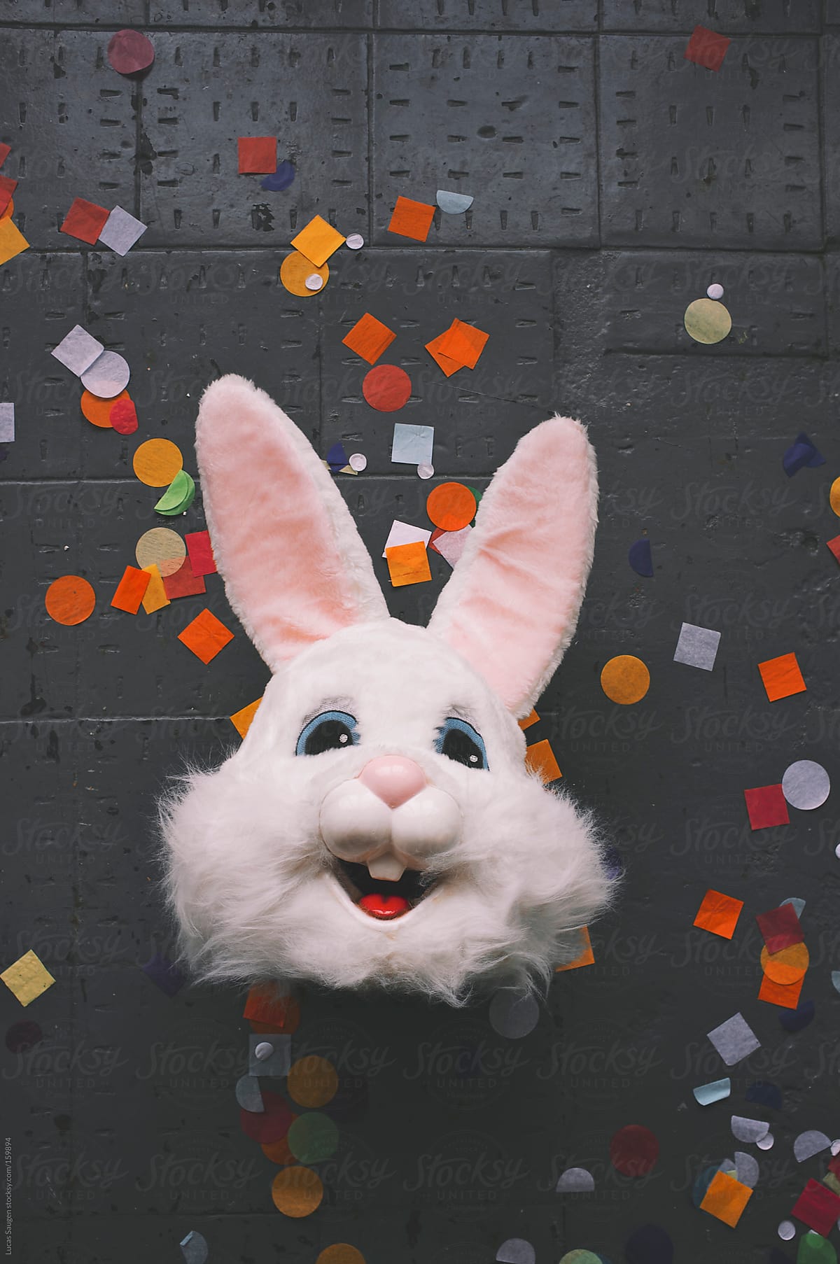 Head to a rabbit costume laying on a concrete floor with colorful confetti.