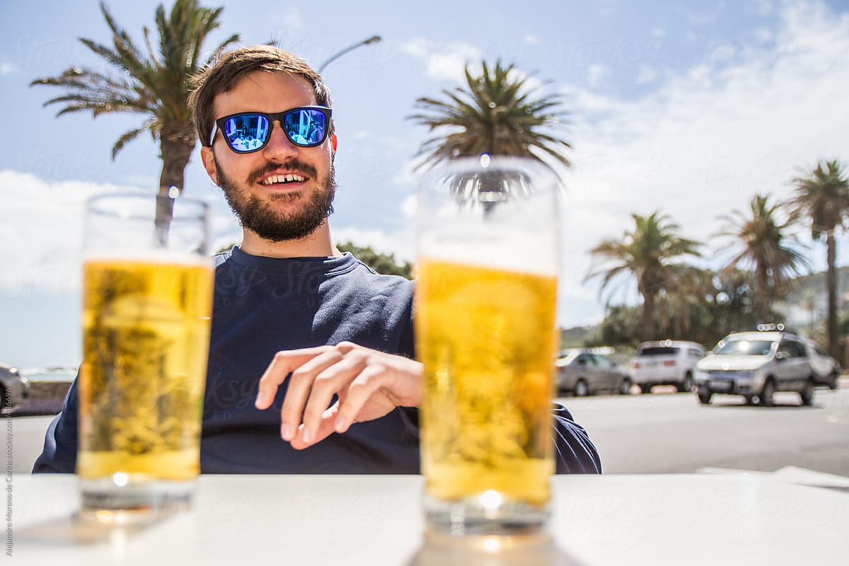 Happy young man enjoying a beer with his friends on the terrace of a bar next to the beach