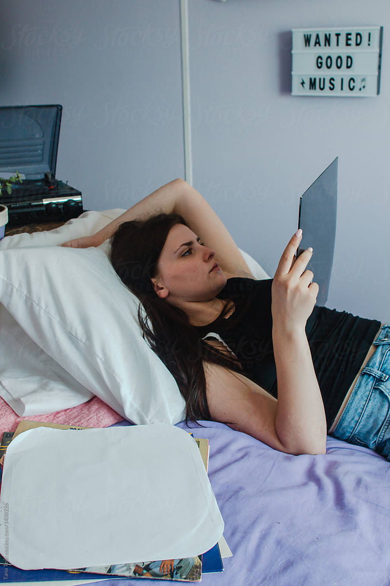 teenager laying on bed looking at record album while listening to music