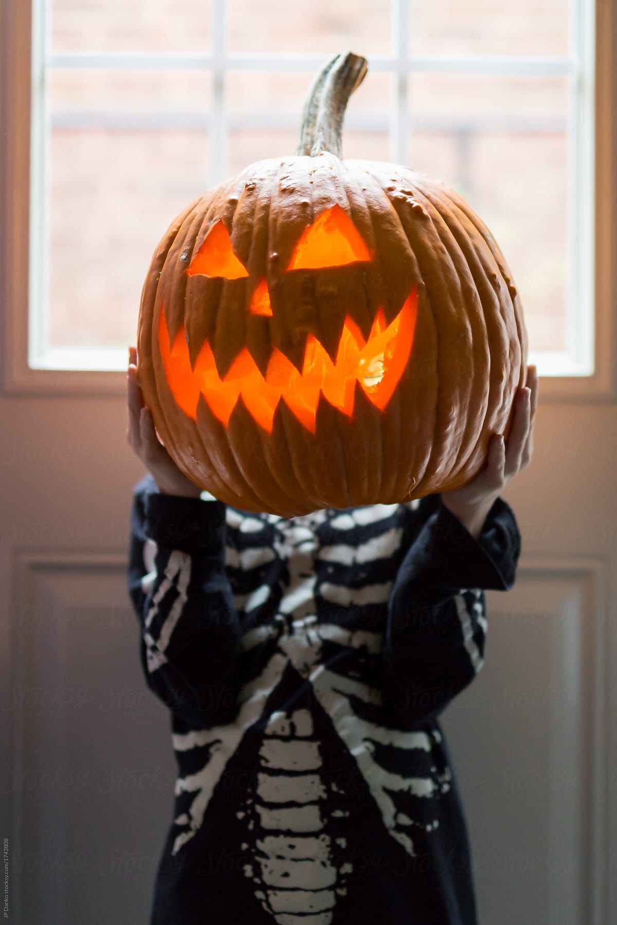 Boy in skeleton shirt holds a glowing Halloween jack-o-lantern u