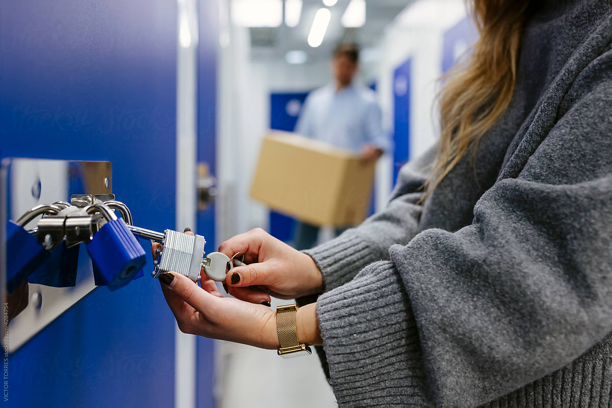 Anonymous woman opening padlocks on a blue door of a storage roo