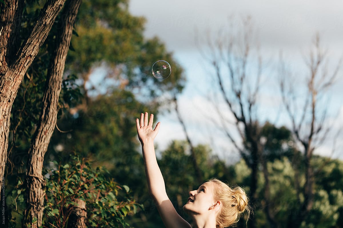 Happy Young Woman Outdoors Reaching For A Bubble Floating Over Her 