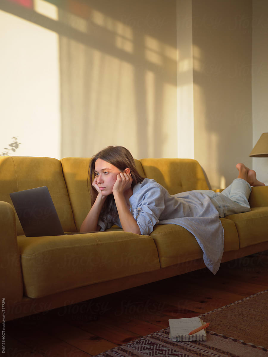 Woman with laptop and notebook laying on the sofa at home