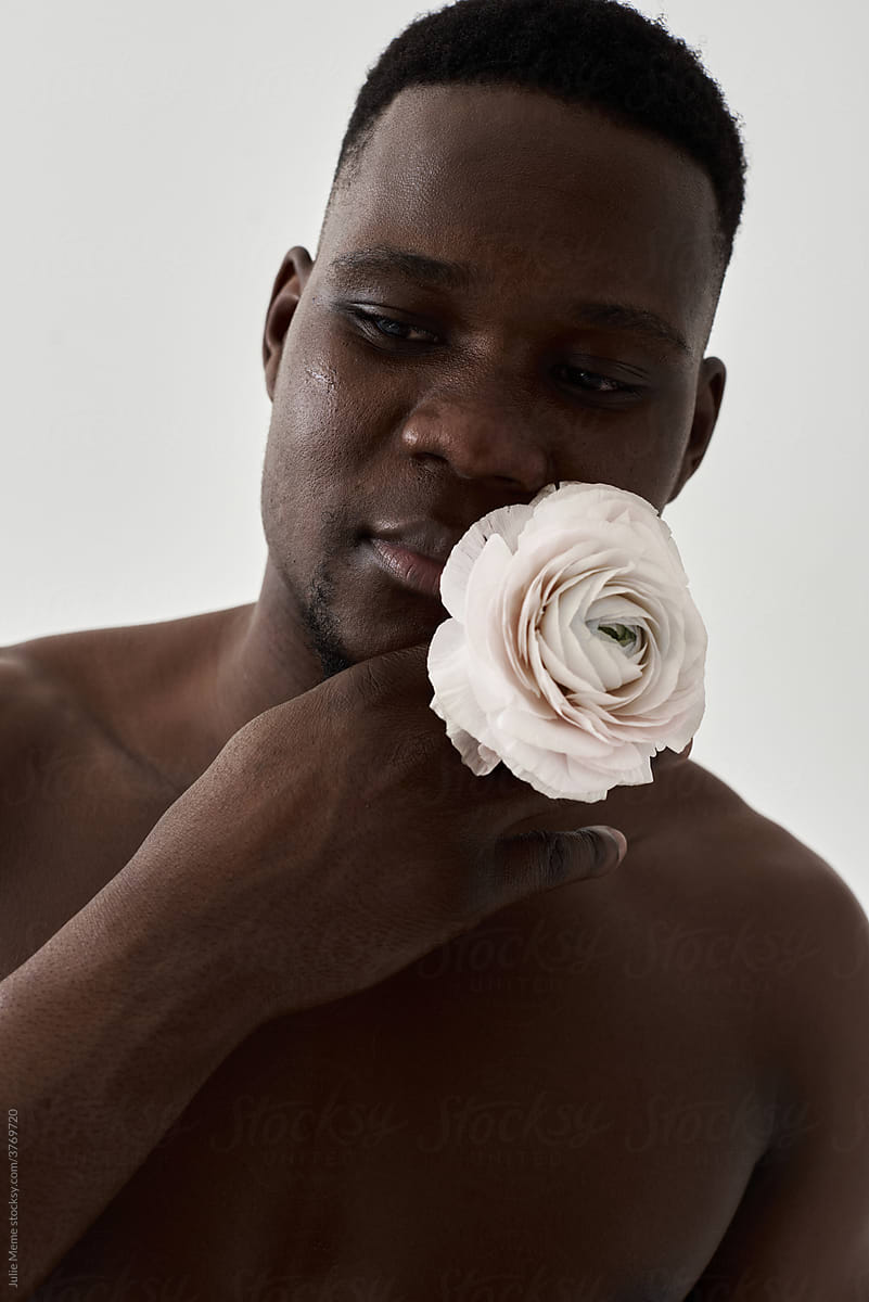 Portrait of a topless african guy with a pale flower near his face