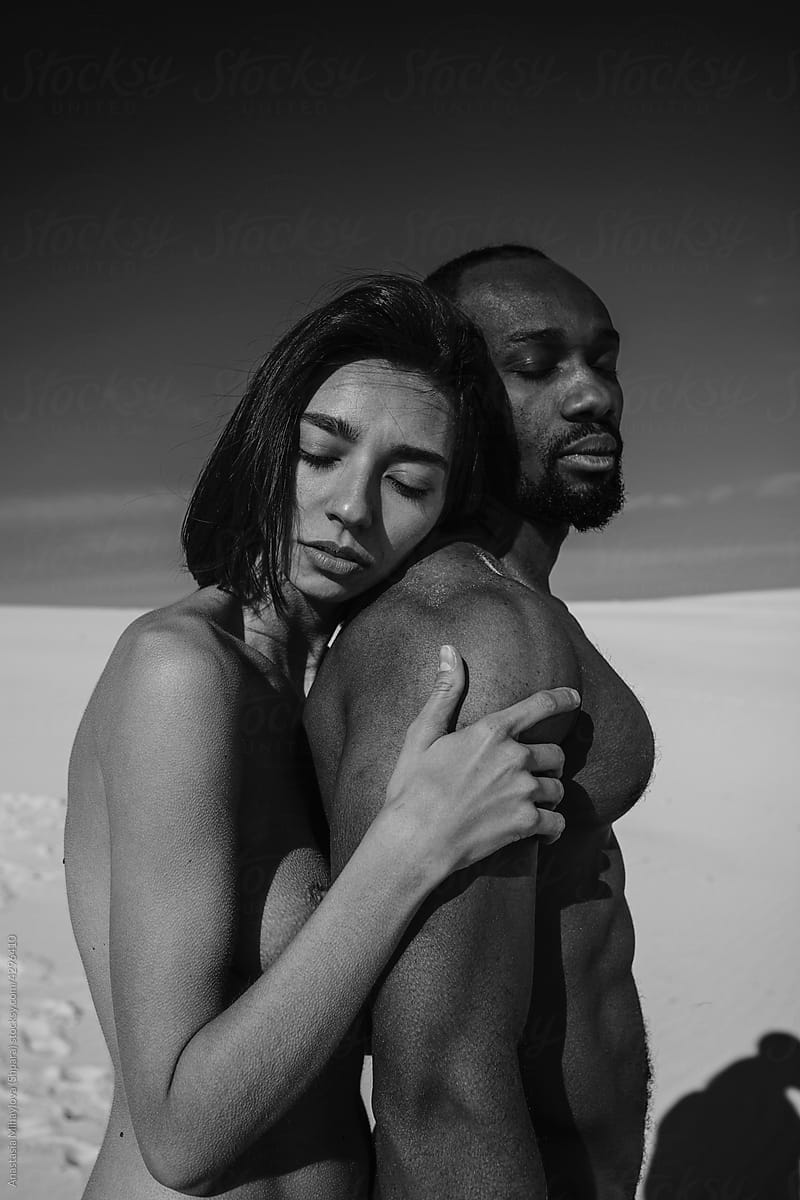 White nude woman hugs an African man from behind.