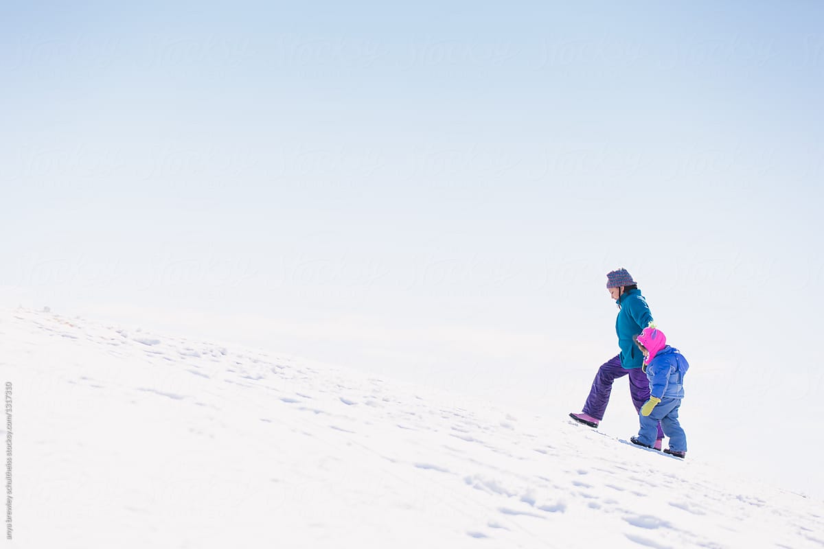 A child helping a toddler walk up a steep snowy hill