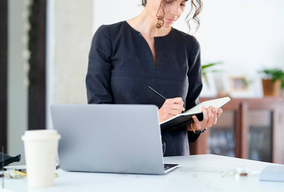 Businesswoman making notes near laptop