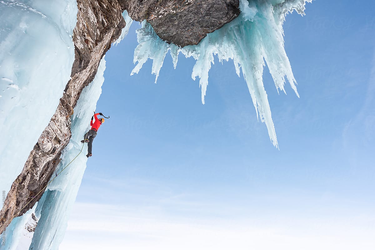 Male alpinist ice climbing on steep frozen waterfall