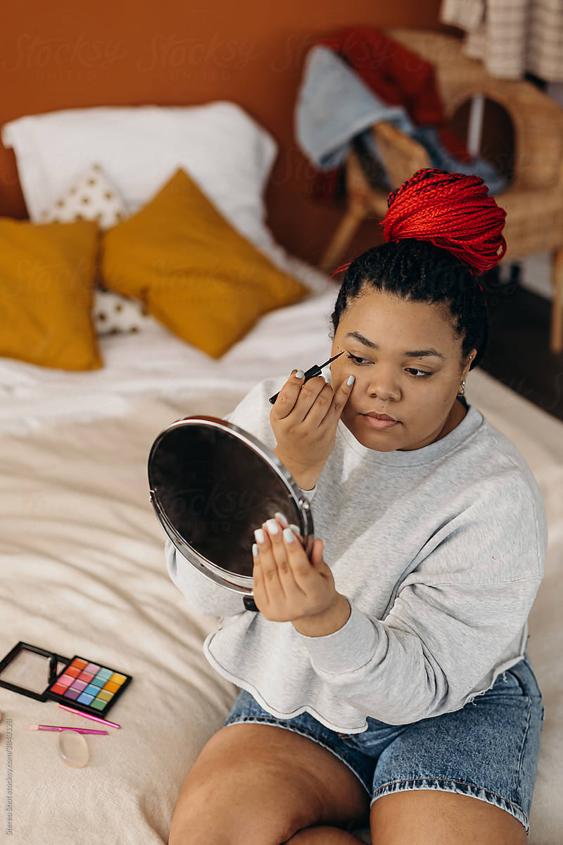focused Black woman applying mascara and looking in mirror