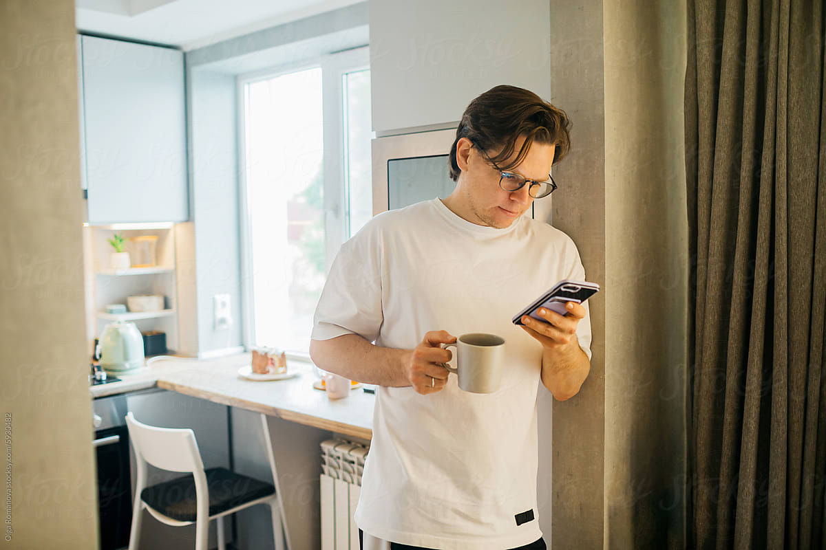 Man holding his smartphone at home in the kitchen, scrolling, texting