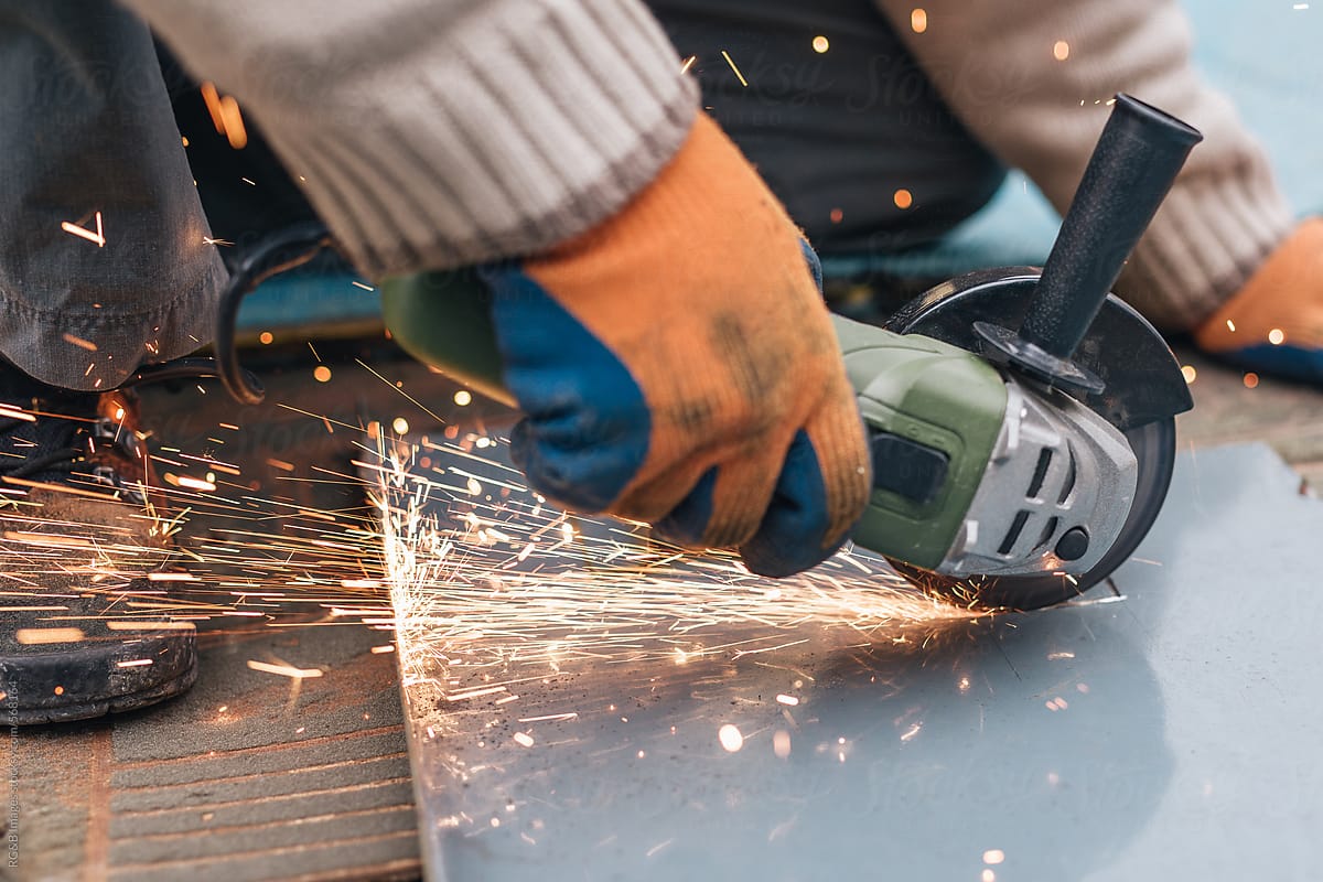 Male worker hands using an angle grinder to cut a tin sheet