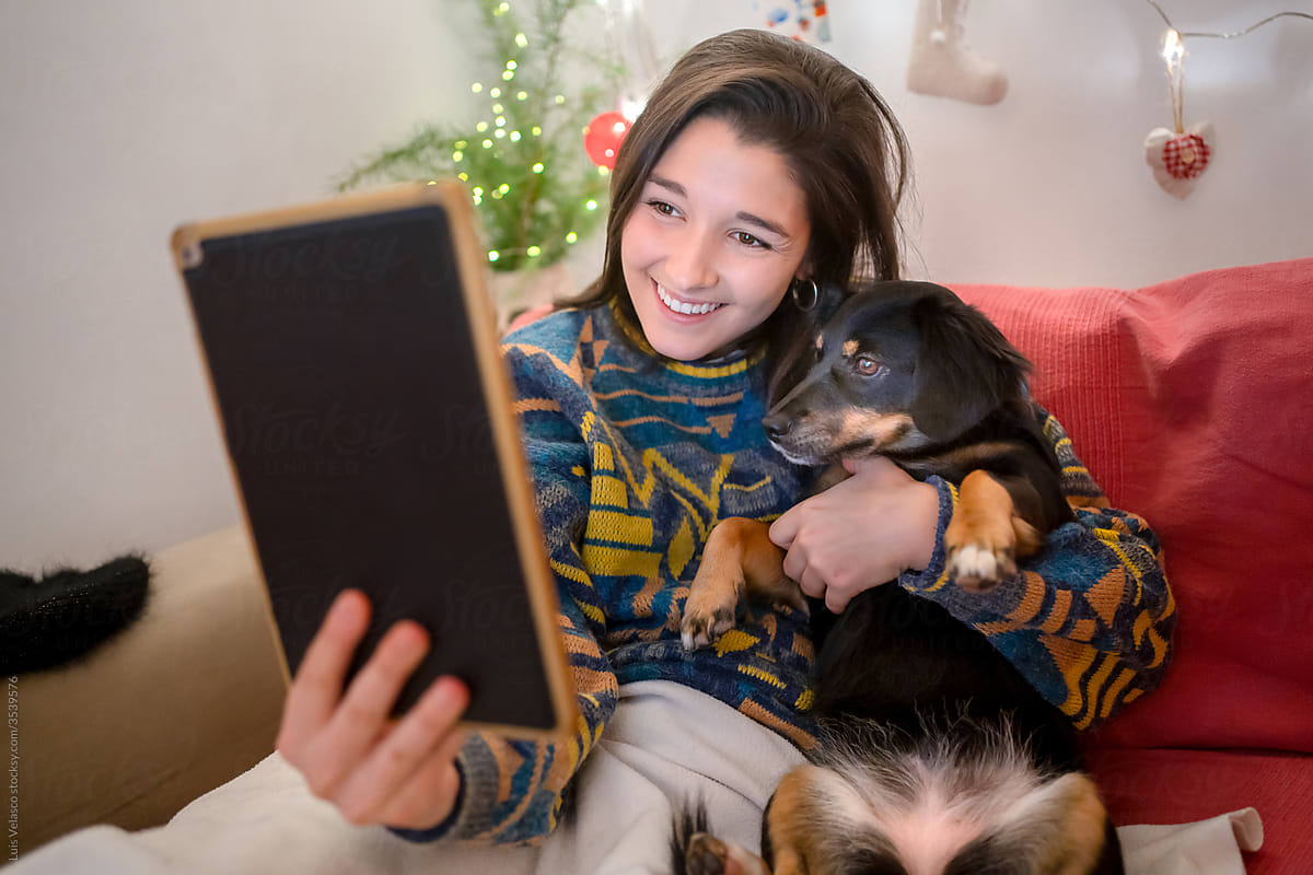 Girl With Her Dog And Tablet Having Isolated Christmas At Home.