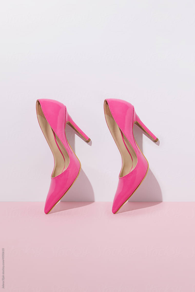 Two pink high heels against pastel wall.