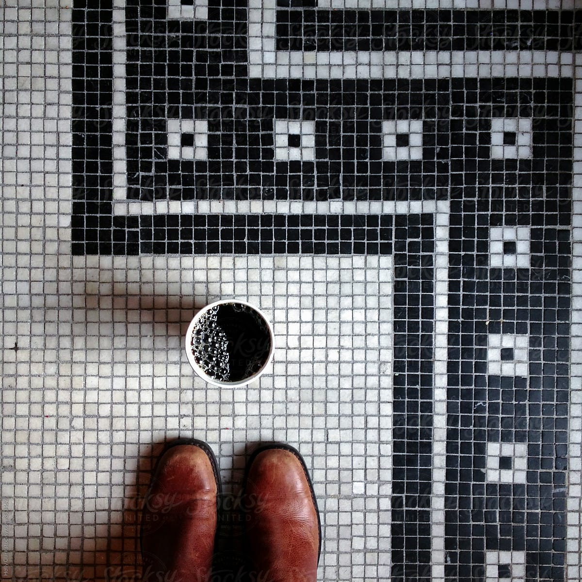 Toes of brown boots in front of coffee cup on a tiled floor at a cafe