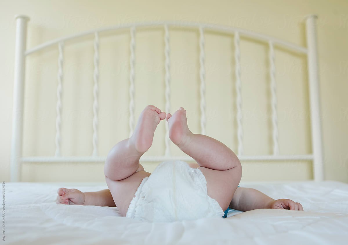 Happy Baby lying on Bed with Diaper with Feet in Air