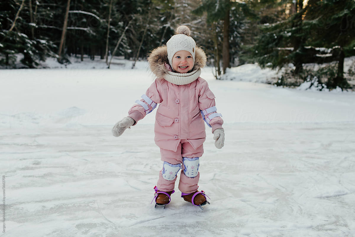 Happy little child learning to skate on ice in forest