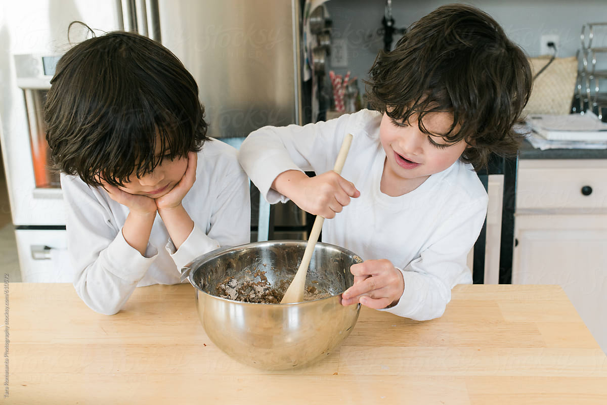 two young boys taking turns stirring cookie batter, making cookies