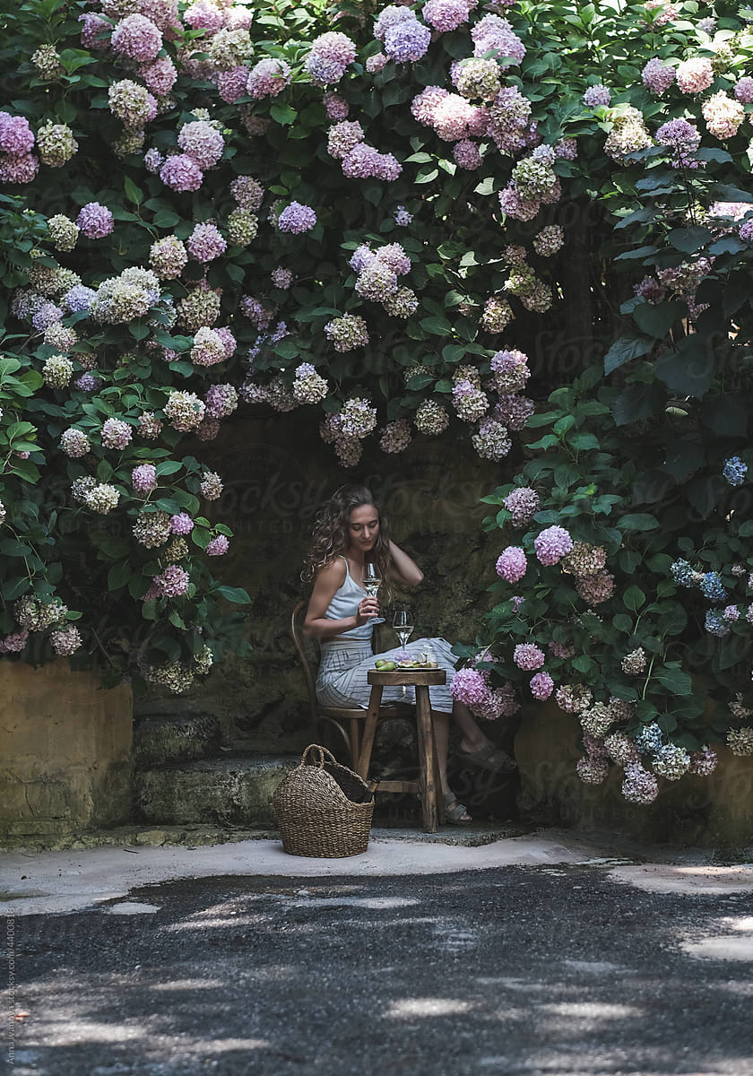 Young woman enjoying wine under blooming hydrangea