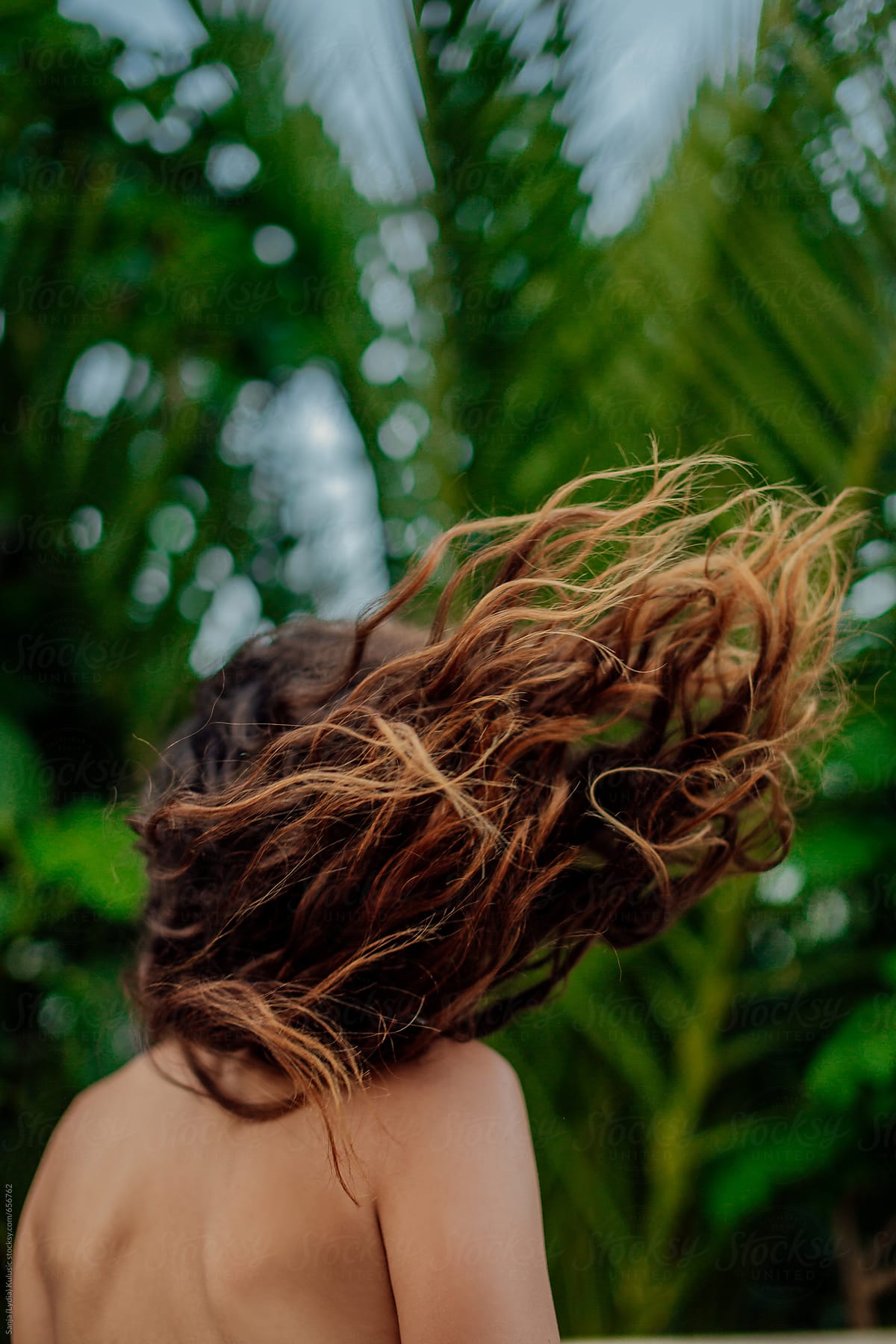 Brown ombre summer hair flying in the air with a green palms in a background