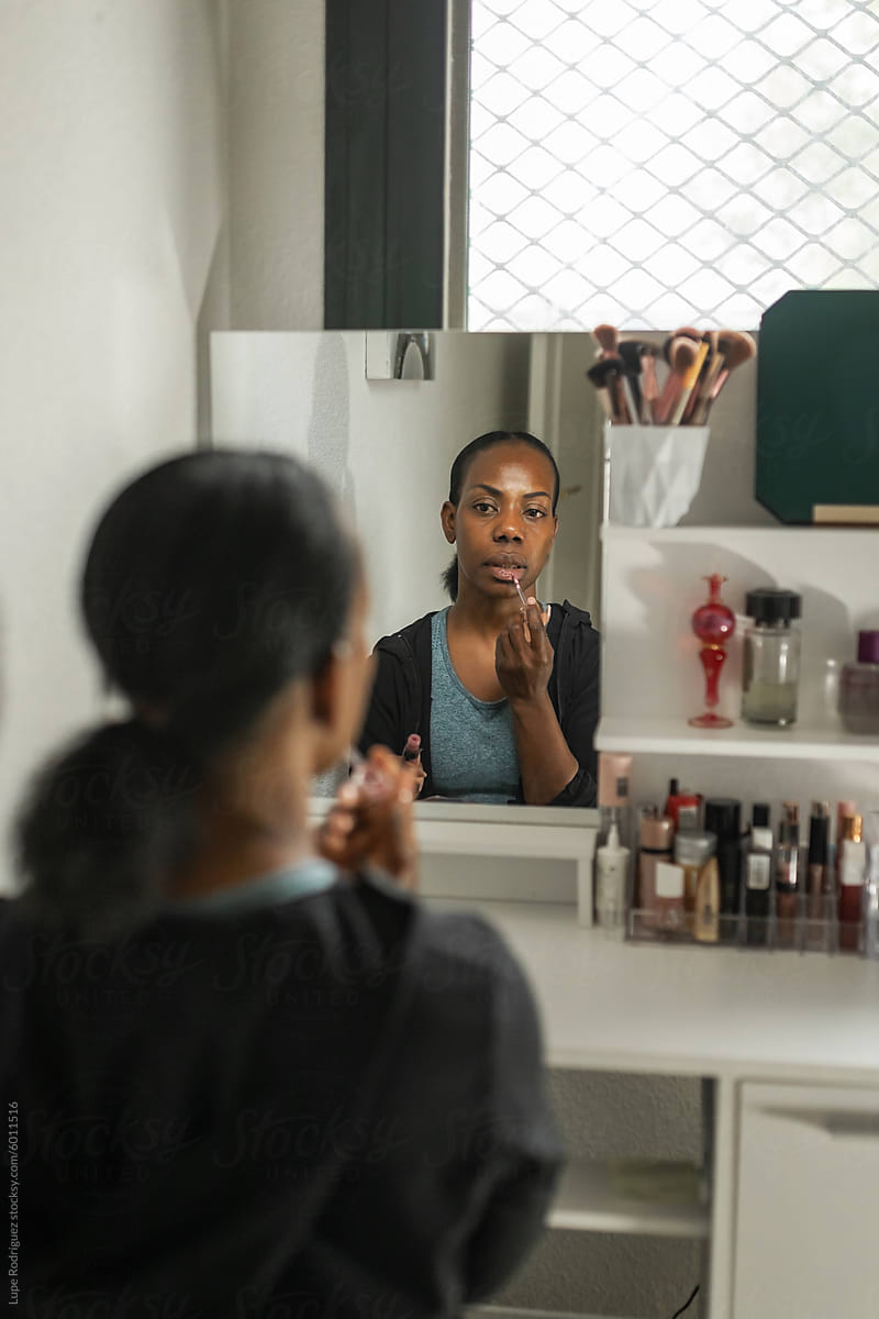 black woman sitting in front of dressing table putting on makeup