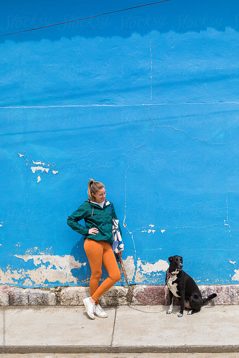 A woman is standing with her dog in front of a blue wall