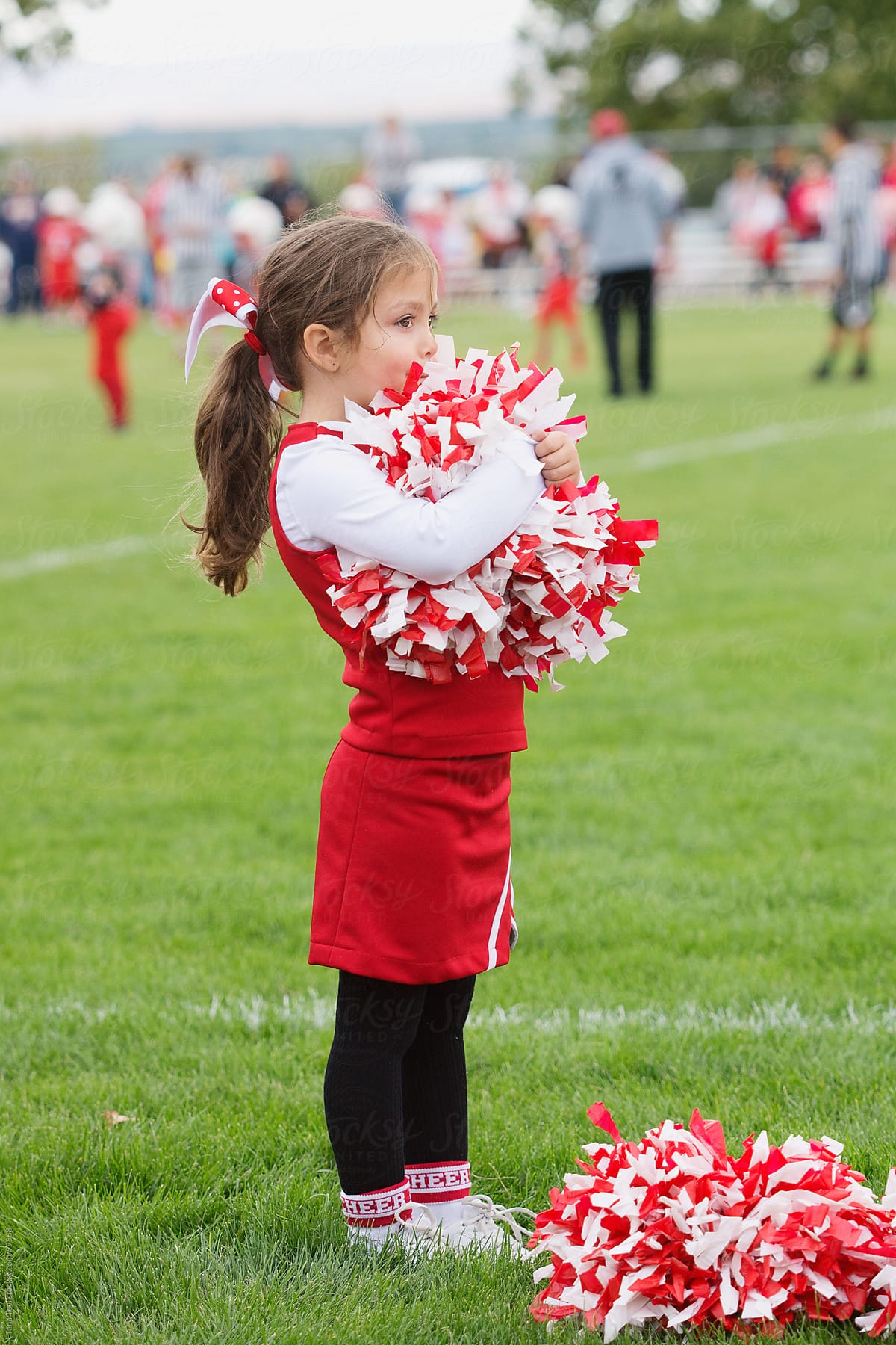 A young cheerleader holds her pom poms and watches the football game