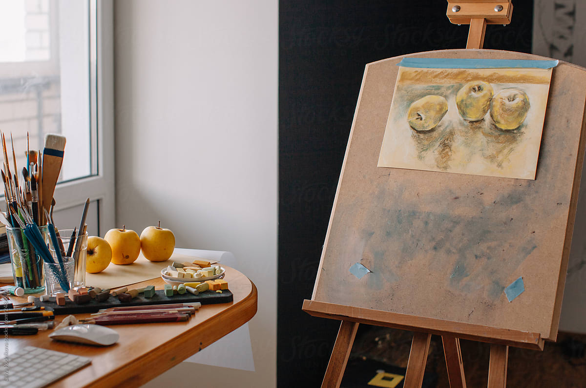 Easel with unfinished drawing of yellow apples in the studio