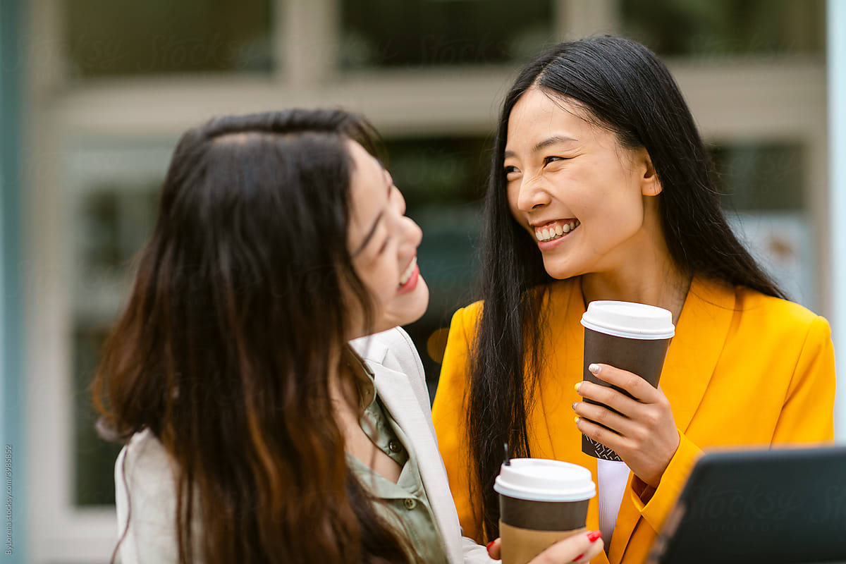 Delighted Chinese women with takeaway coffee laughing on street