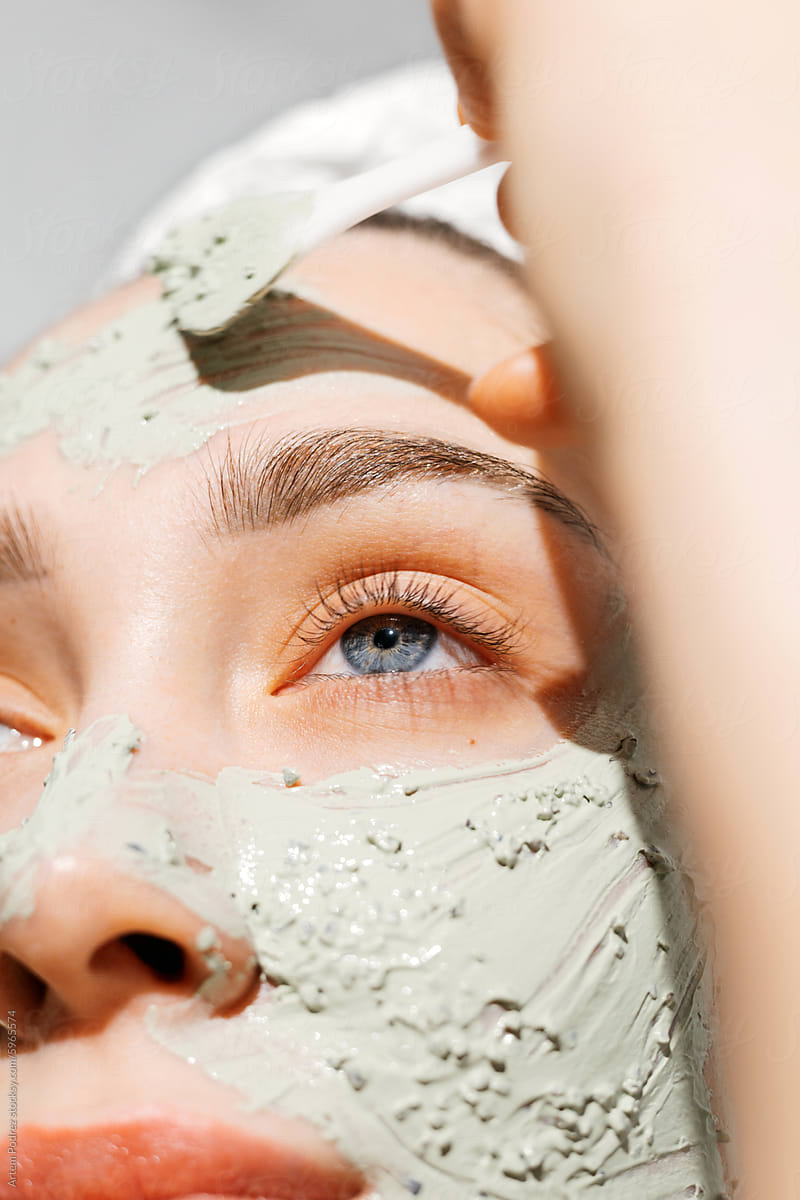 Close-up Woman applies Revitalizing Facial Clay Mask Treatment