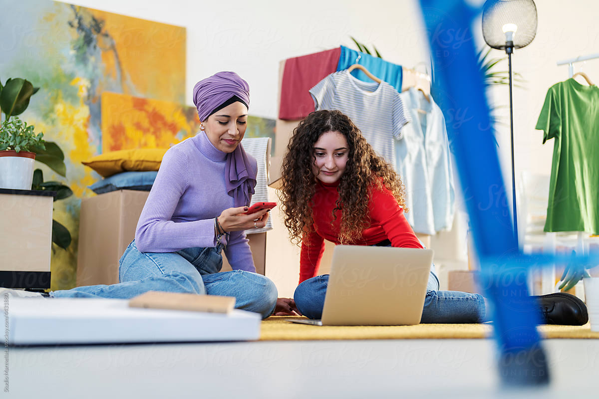 Cheerful diverse women using laptop in new apartment