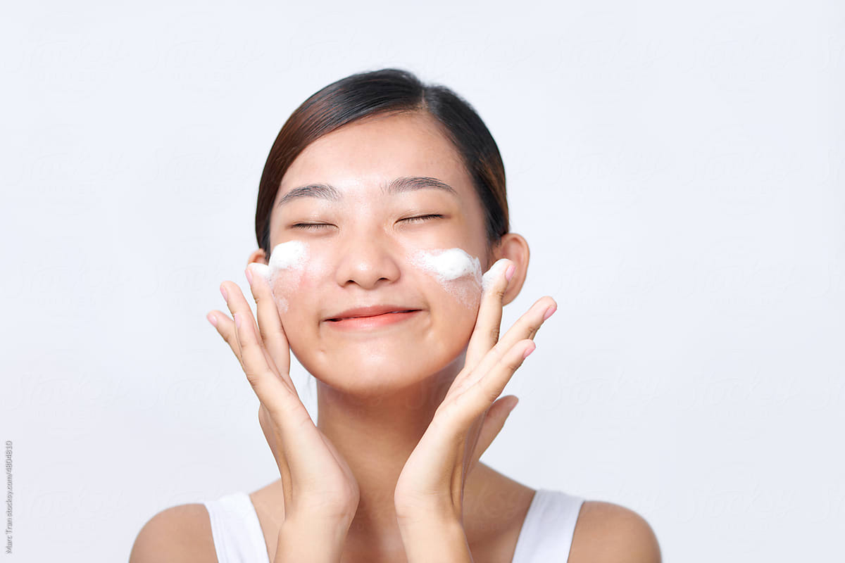 Satisfied girl applying cleansing beauty product on cheeks closed eyes