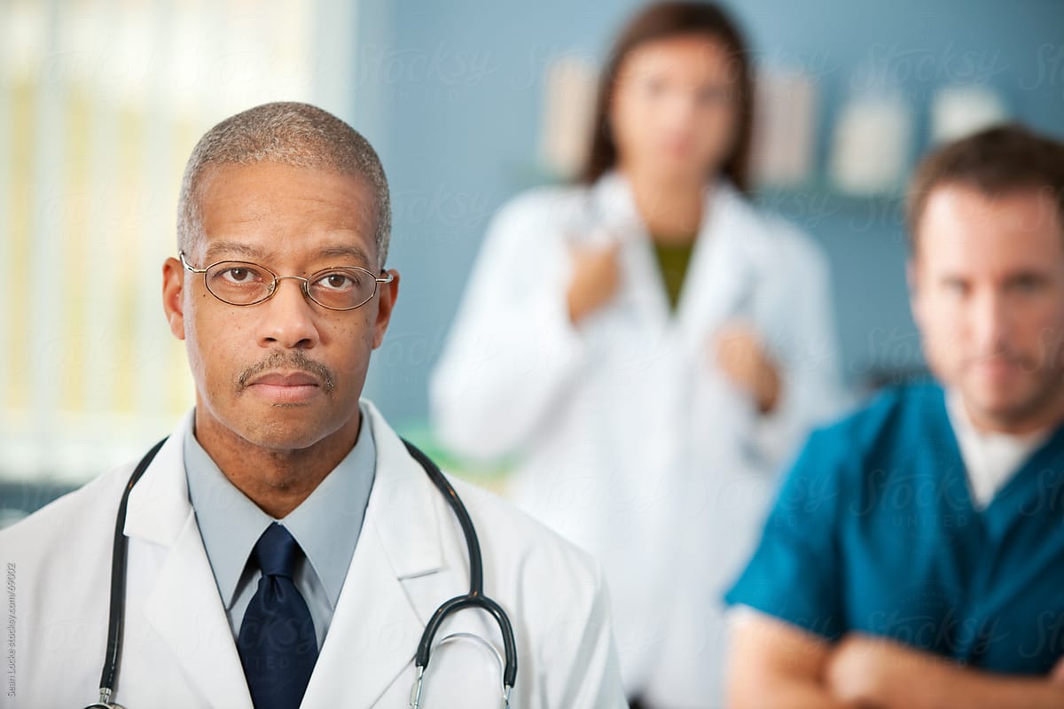 Exam Room: Concerned Male Physician with Team Behind