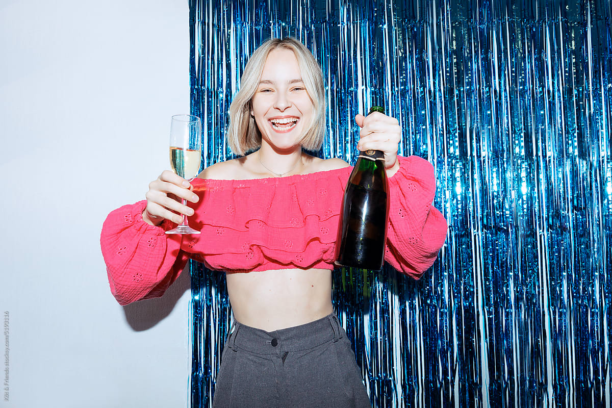 Excited Blonde Woman Posing With Champagne Bottle And Glass