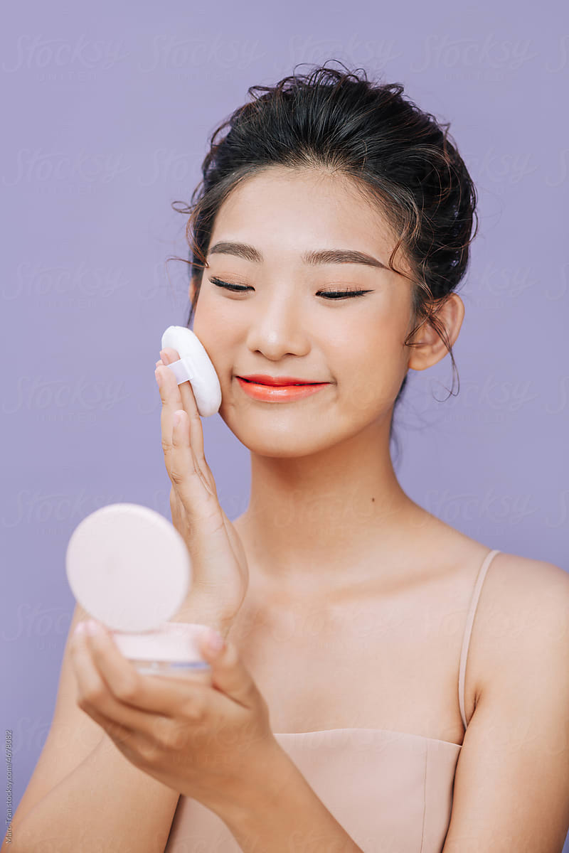 Beautiful Asian woman using powder puff to makeup