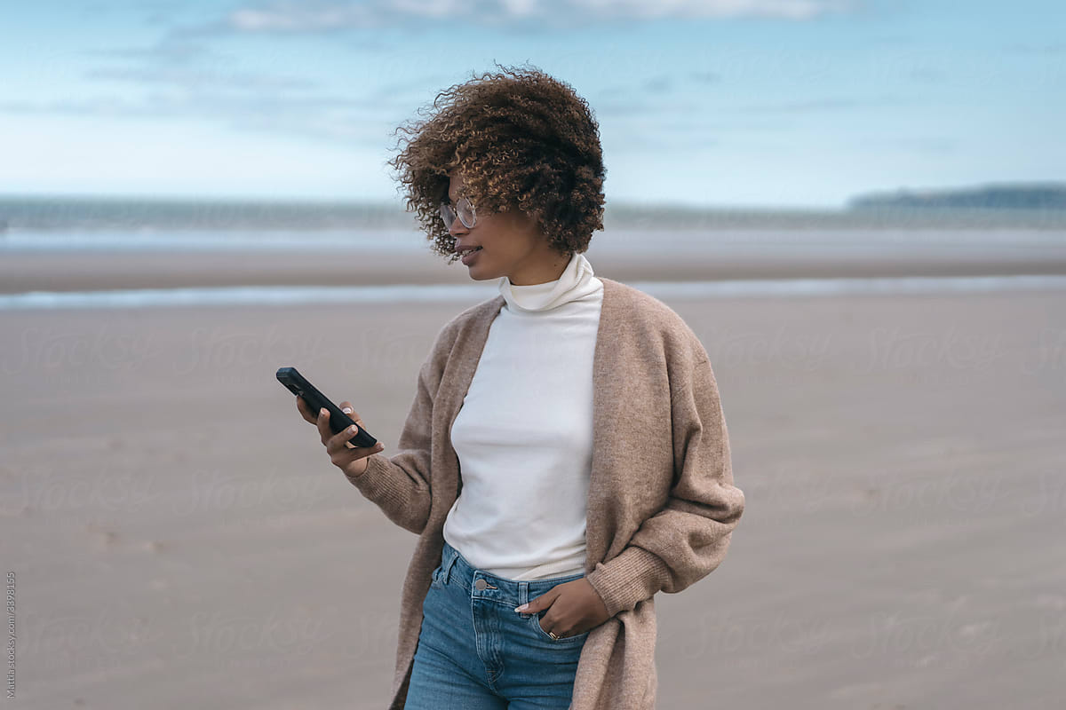 Black Woman Uses a Mobile Phone on the Beach