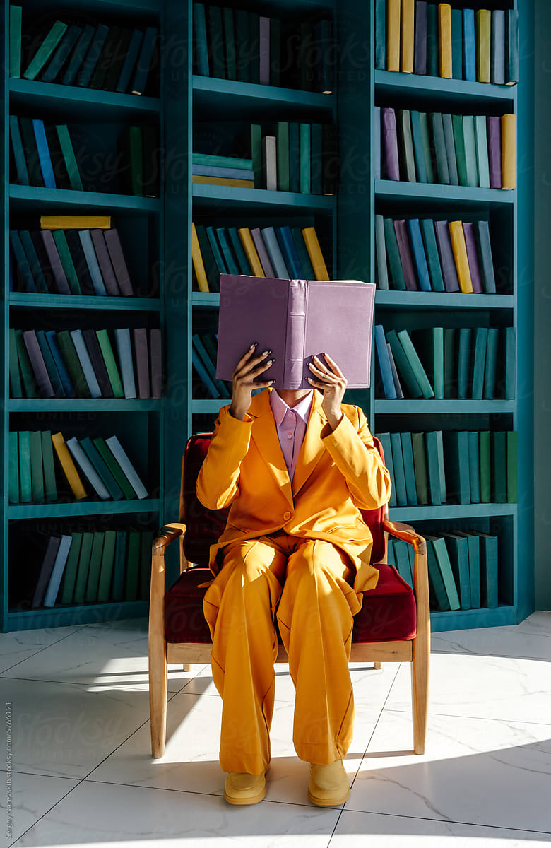 Woman in suit covering face with opened book on armchair