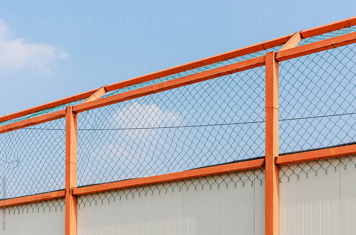 Sunny sky and orange steel fence close-up.