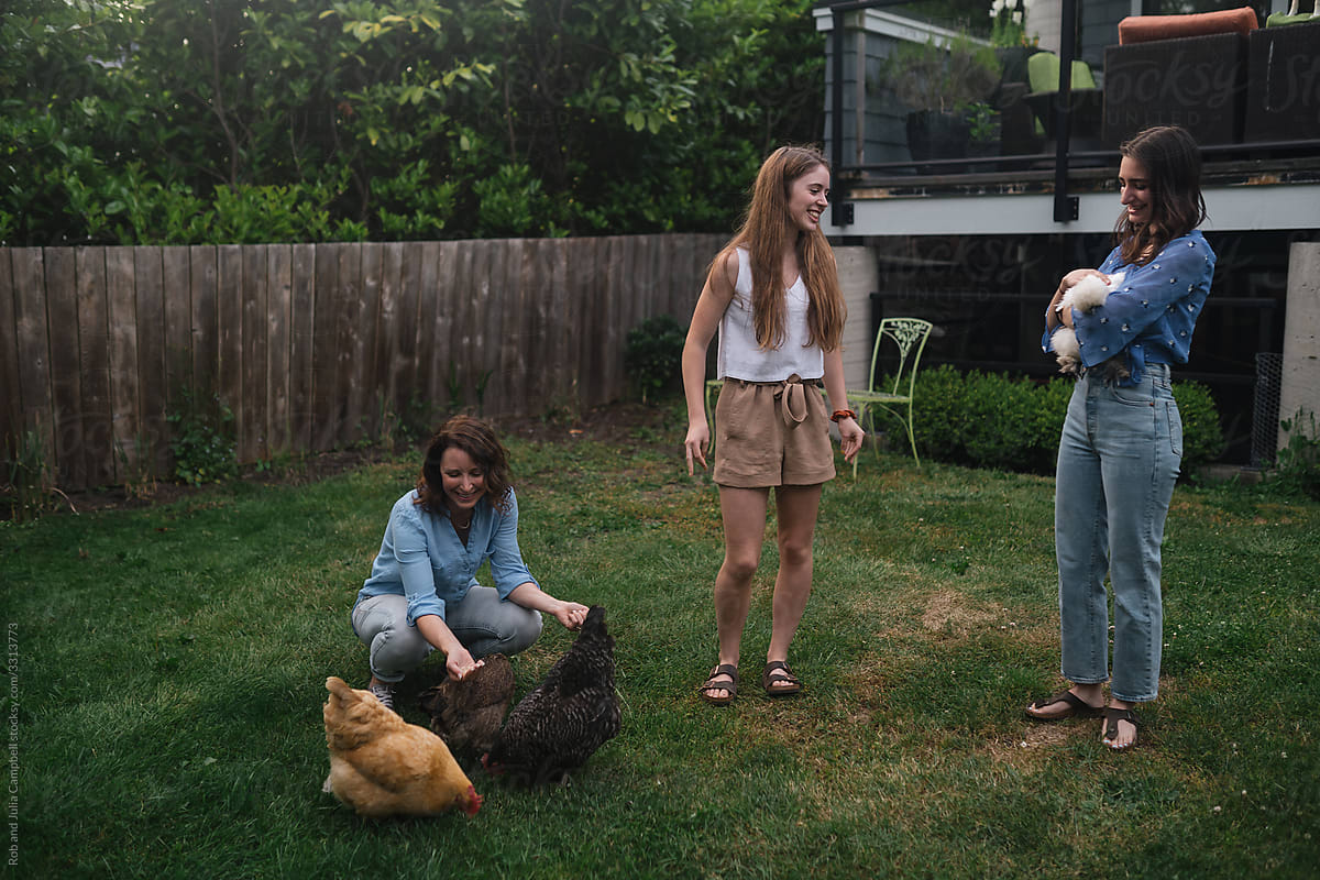 Mom and adult daughters hanging out with chickens in the backyar