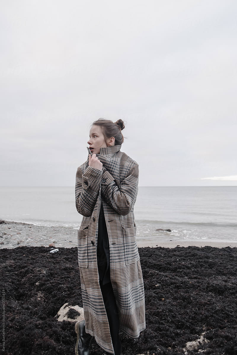 A girl walks along the beach and wraps herself in a coat next to the cold sea