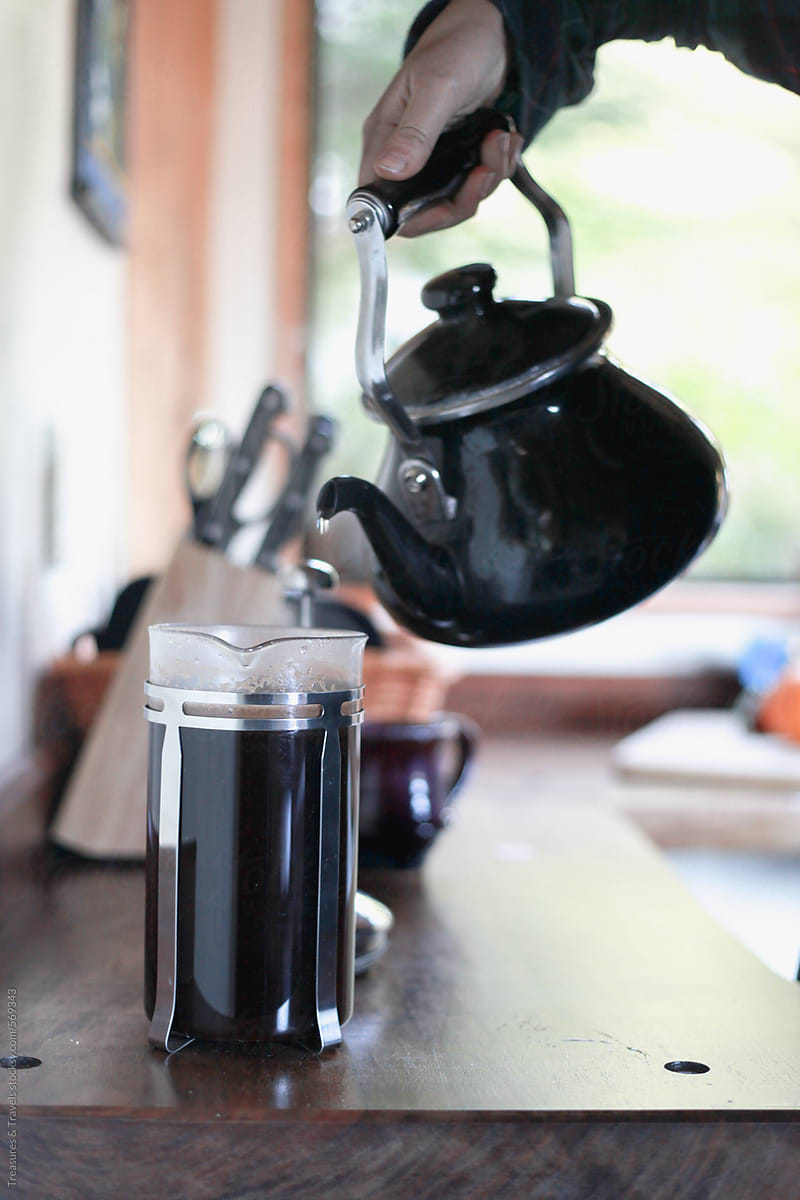 hand pours coffee into mug from a french press on table