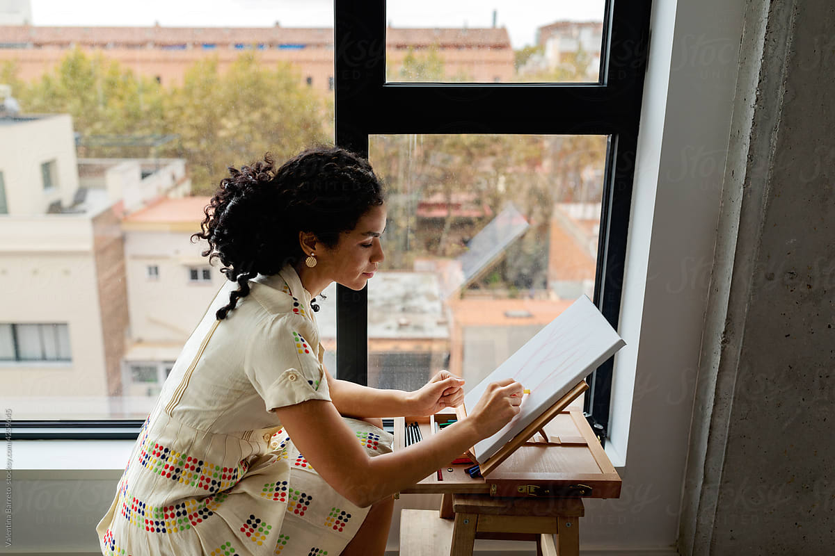 Woman painter painting picture near window