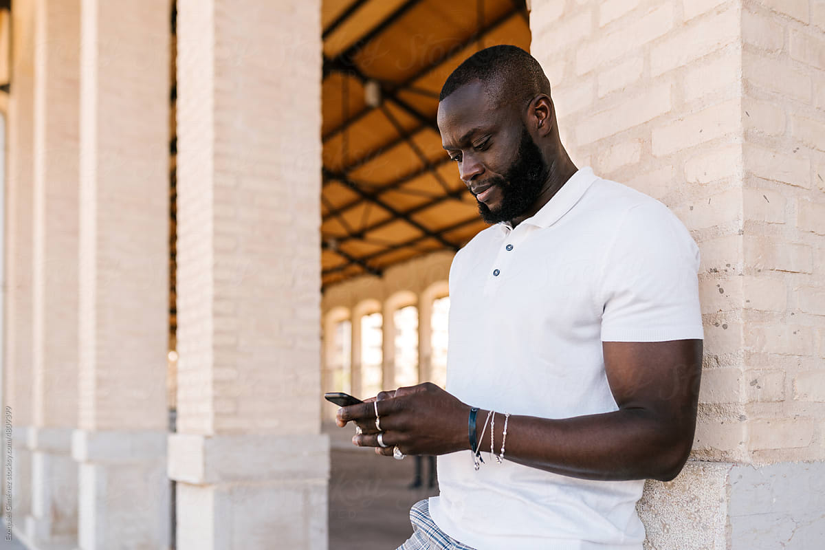 Bearded black guy using smartphone near brick building